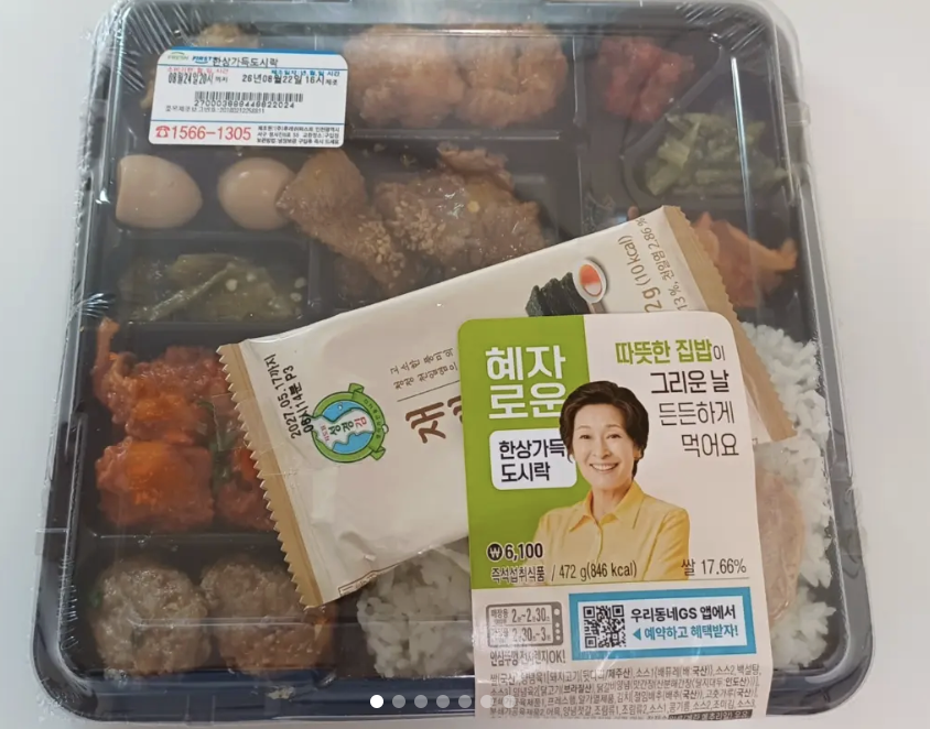 A GS25 Hyeja-roun Hansang Gadeuk dosirak lunchbox with its label showing 6,100 won and 472g, 846 kcal — a segmented tray of rice, fried chicken pieces, boiled eggs, meatballs and vegetable side dishes