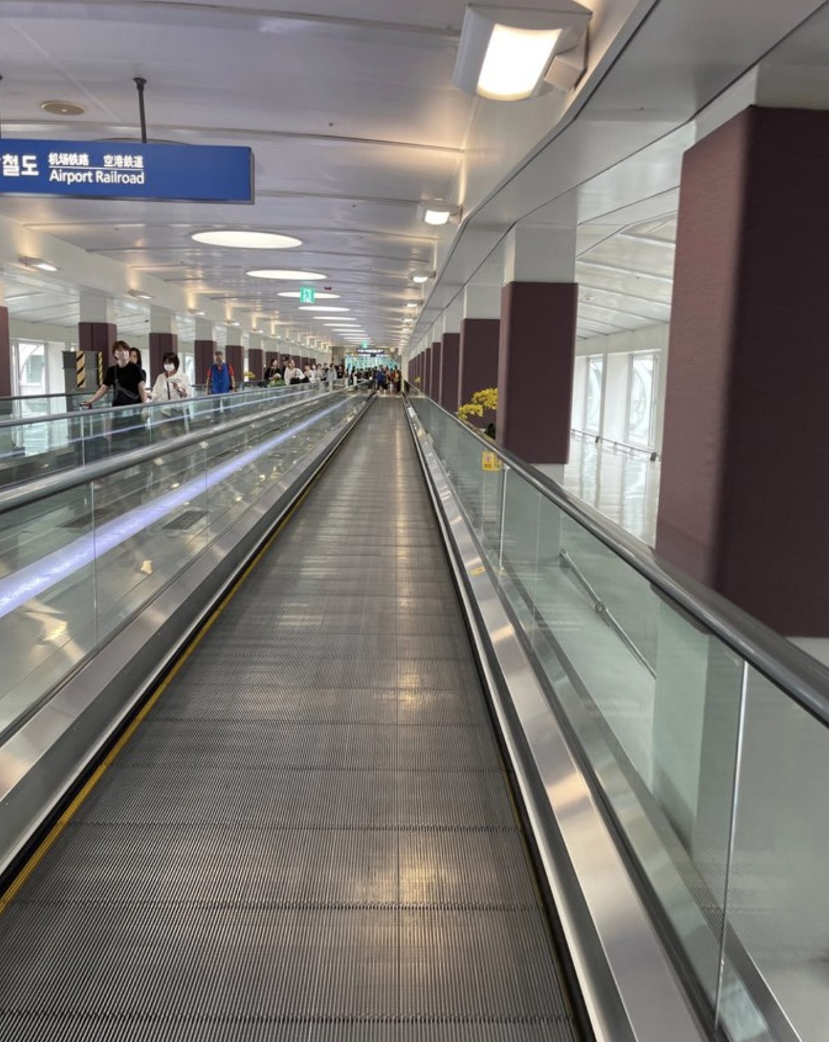 Long moving walkway in a corridor at Incheon Airport with an Airport Railroad sign overhead