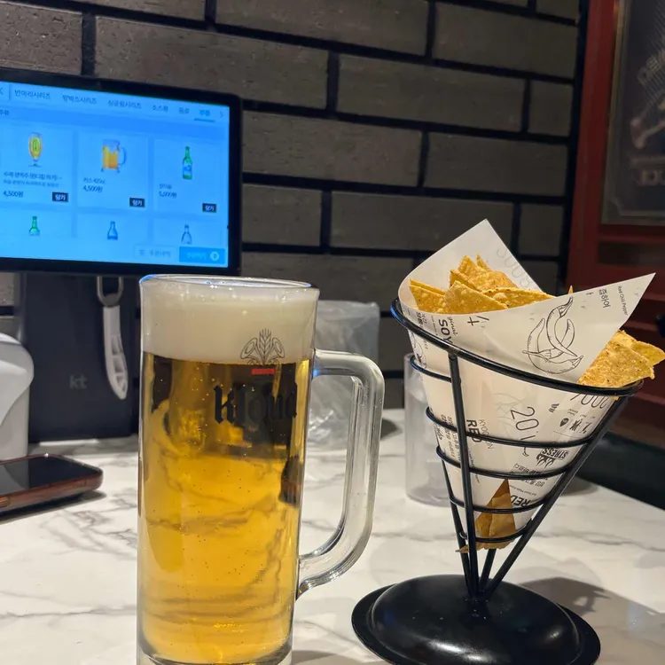 A mug of draft beer and a cone of tortilla chips on a marble table, with the store's ordering tablet visible behind