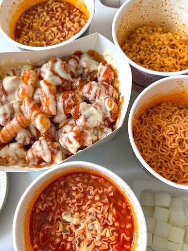 A box of Cheogajip supreme yangnyeom chicken surrounded by bowls of buldak instant noodles and pickled radish