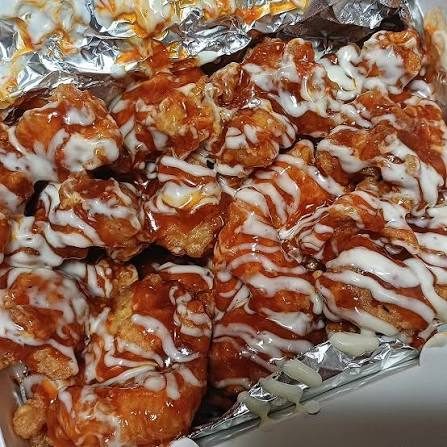 A foil takeout tray of Cheogajip boneless supreme yangnyeom chicken seen from above, white sauce drizzled in lines across red-glazed pieces
