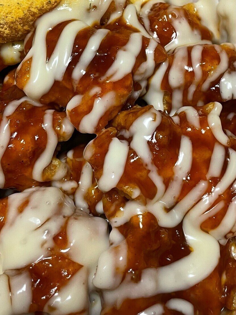 Close-up of Cheogajip supreme yangnyeom chicken: glossy red gochujang glaze with thick white cream sauce drizzled across it in ribbons